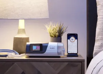 Airsense 11 machine on a nighstand next to bed with lamp and phone